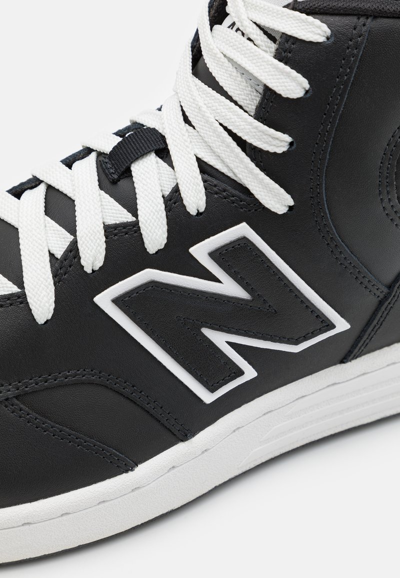 Schwarzer High-Top-Sneaker aus Leder mit weißen Schnürsenkeln, ausgestattet mit einem markanten weißen 'N'-Logo und strukturierten Akzenten an der Seite.