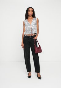 Silberner Pailletten-Fransenoberteil mit V-Ausschnitt, kombiniert mit schwarzen hochtaillierten Jeans und einer roten Schultertasche. Das Model trägt schwarze spitze Pumps.