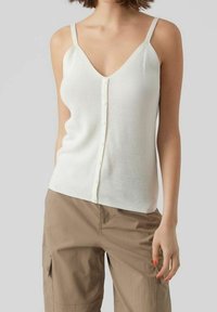 Canottiera bianca a coste con scollatura a V, con fronte a bottoni e spalline sottili. Abbinata a pantaloni cargo marrone chiaro.
