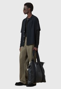 Schwarzes Kurzarmhemd, grüne weite Hose und eine glänzende schwarze Leder-Tasche mit Stoffträgern. Strukturierte Muster auf dem Hemd.