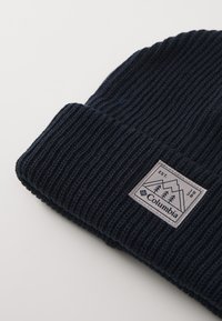 Granatowa czapka beanie z prążkowanego dzianiny z podwiniętym brzegiem, z kwadratową naszywką logo Columbia z górami i drzewami.