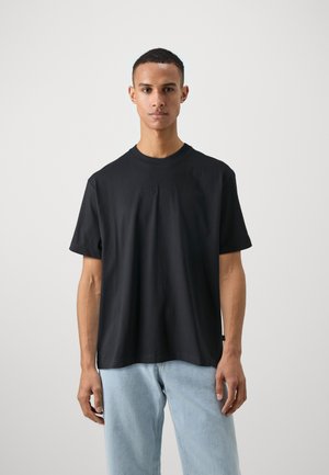 Zwart katoenen T-shirt met korte mouwen, ronde halslijn en subtiele reliëflogo op de borst, gecombineerd met lichtblauwe denim jeans.