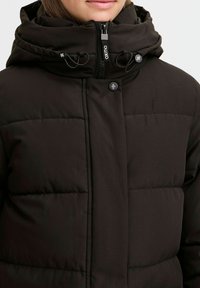 Black puffer jacket with a hood, featuring a zip closure, snap buttons, and elastic drawstrings. Smooth fabric with stitched paneling.