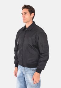 Giubbotto bomber nero con chiusura a zip, colletto, due tasche frontali e polsini a coste. Realizzato in tessuto morbido e leggero.
