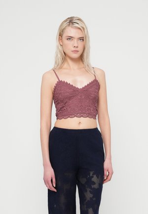 Burgunderfarget blondetruse med bølgete kanter og blomsterdekorer, brukt sammen med marineblå bukser med gjennomsiktige blomsterdetaljer.