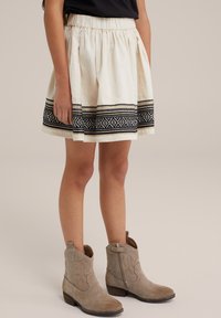 Valkoinen puuvillahame, jossa on musta geometrinen kirjailtu reuna, joustava vyötärö. Yhdistetty vaaleanruskeisiin tekstuuriankkureihin.