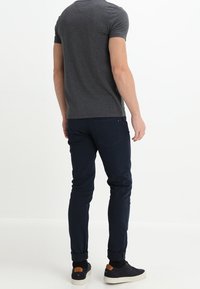 Camiseta gris de manga corta para hombre combinada con jeans ajustados de tiro oscuro y zapatillas negras, mostrando un ajuste relajado y un diseño minimalista.