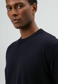 Marineblauwe gebreide trui met een ronde hals, gemaakt van gladde stof, met geribbelde accenten bij de kraag en manchetten, minimalistisch ontwerp.