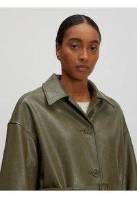 Olijfgroene kunstleren jas met een brede kraag, twee knopen aan de voorkant en een ceintuur in de taille. Heeft een gladde, licht glanzende textuur.