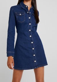Jeansskjortklänning i mörkblått, med långa ärmar, knappstängning fram, två bröstfickor och silverfärgade knappar längs knäppningen.