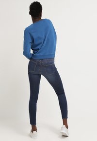 Modrá mikina s uvolněným střihem, vyrobená z bavlny, s žebrovanými náplety, kombinovaná s tmavě modrými skinny džíny a bílými teniskami.