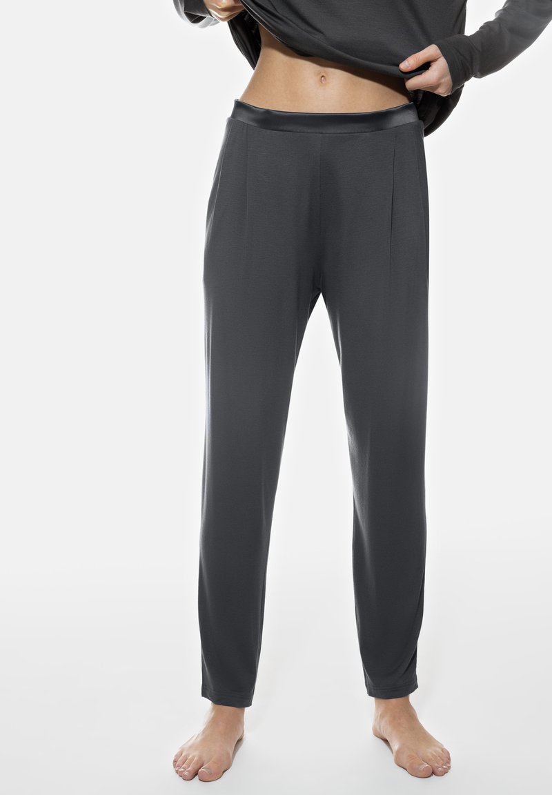 Donkergrijze, lichte broek met een gladde satijnen tailleband, met een ontspannen pasvorm en geplooid ontwerp, gedragen op blote voeten.