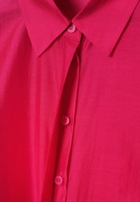 Chemise rose vif à col avec boutons sur le devant, montrant une texture de tissu lisse et des détails de couture soignés.