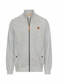 Veste sweat quiltée grise avec un col haut, fermeture éclair à l'avant, poches latérales et un patch en cuir. Texture lisse et design décontracté.