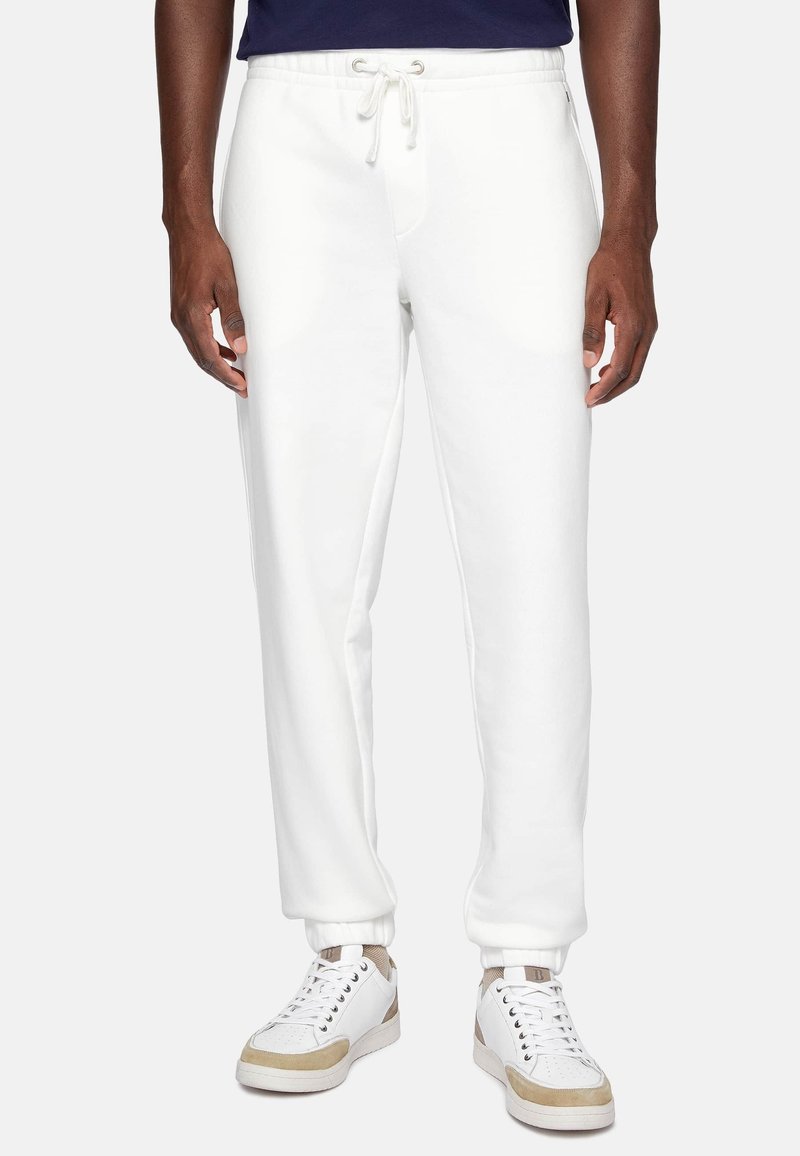 White sweatpants with ribbed cuffs, drawstring waist, side pockets, and smooth texture, paired with white sneakers featuring beige accents.
