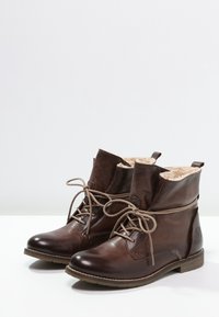 Braune Leder-Stiefeletten mit Kunstfell-Futter, runder Zehenform, Schnürdesign, niedrigem Absatz und charakteristischem Logo-Detail an der Seite.