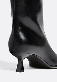 Bottine en cuir noir avec un design épuré, bout pointu et un talon carré et élancé. Texture lisse avec un minimum de détails.