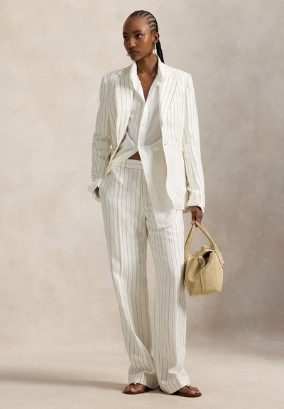 Λευκή κοστούμι με λεπτές ρίγες, με σακάκι ραμμένο κατ' εξατομίκευση και παντελόνι με φαρδιά μπατζάκια, σε συνδυασμό με λευκό πουκάμισο και μπεζ τσάντα, συμπληρωμένο με κομψά σανδάλια.