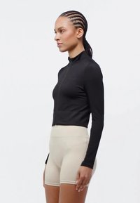 Black long-sleeve zip-up top with a high collar, paired with beige high-waisted shorts. Smooth texture, fitted design.