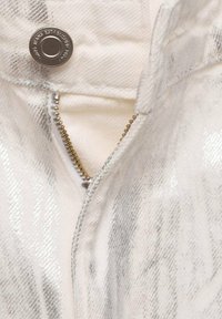 Bela zip-up jakna s sijočim srebrnim črtastim vzorcem. Ima kovinski gumb na zapiranje in zlato zadrgo na sprednji strani.