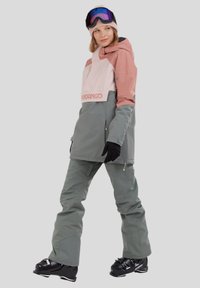 Isolerad skidjacka och byxor i ljusrosa och grå toner, med huva, fickor med dragkedja och en vattentät yta.