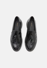 Schwarze Lackleder-Lederschuhe mit einem Quastenakzent an der Vorderseite, die ein gewelltes Design entlang der Kanten und eine strukturierte Innensohle aufweisen.