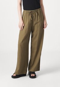 Lichte olijfgroene wijde broek met een elastische tailleband en trekkoord, gecombineerd met zwarte platform sandalen.