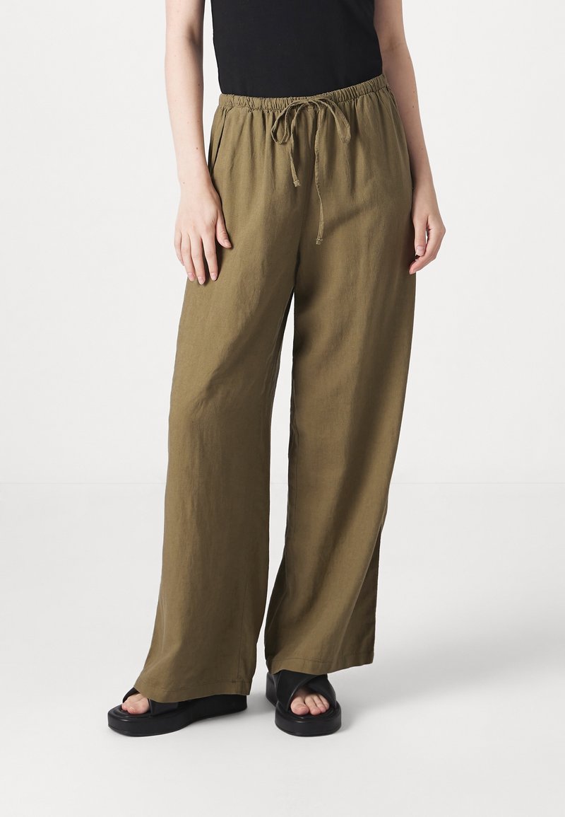 Lichte olijfgroene wijde broek met een elastische tailleband en trekkoord, gecombineerd met zwarte platform sandalen.