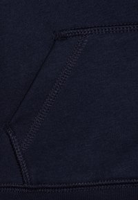 Navy blue fabric featuring a textured surface with visible stitching details. Includes a front pocket with reinforced edges.