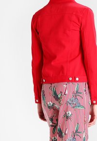 Röd denimjacka med en figursydd design, tryckknappar vid midjan och en strukturerad krage, kombinerad med en kjol med blommönster och randig design.