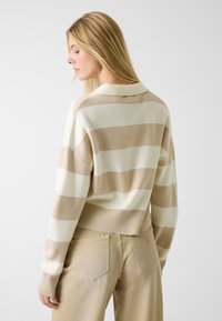 Pull rayé beige et blanc avec un ourlet et un col côtelés, texture légère, avec une petite étiquette de marque au dos.