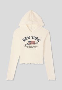 Hoodie bianco cropped con texture a coste, presenta una grafica frontale con la scritta "NEW YORK", una bandiera americana e un orlo scallop.