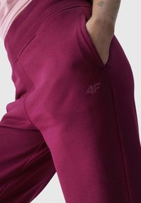 Bordeauxfarbene Sweatpants aus weichem Material, mit einer Seitentasche und einem dezenten Logo auf dem Oberschenkel. Sanfte Textur, elastischer Bund.