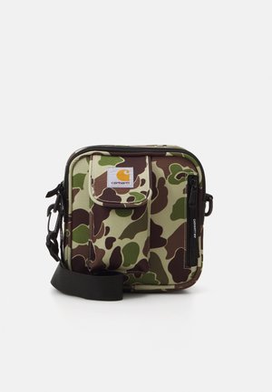 Sac bandoulière Carhartt imprimé camouflage vert et marron avec poche avant, fermeture éclair noire et sangle noire réglable sur fond blanc.