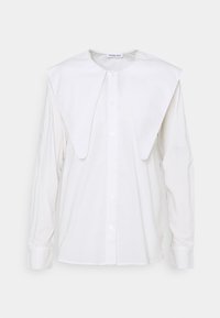 Camicia bianca a maniche lunghe con un ampio colletto arrotondato. Realizzata in un tessuto morbido, con chiusura a bottoni sul davanti e polsini aderenti.