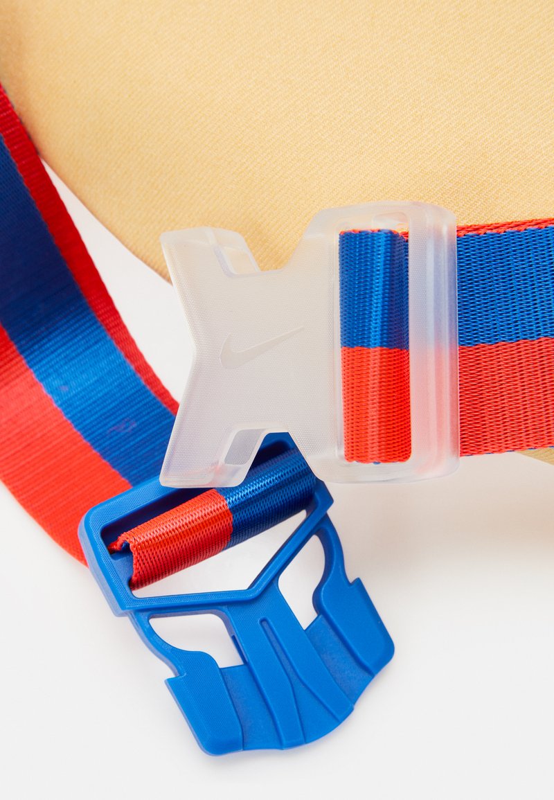 Ceinture Nike avec une sangle en tissu rayée bleu, rouge et bleu clair, dotée d'une boucle translucide. La boucle présente un logo imprimé visible.