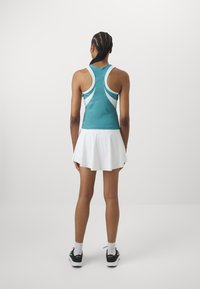 Teal sportieve tanktop met witte accenten, gecombineerd met een witte uitlopende rok. Met een racerback ontwerp en lichtgewicht stof. Zwarte sneakers.