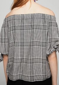 Off-shoulder top i sort/hvid plaid med elastisk halsudskæring, pufærmer og en løs, afslappet pasform. Tekstureret vævet stof.