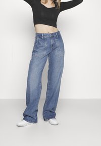 Breda benblå jeans i denim. Har framfickor, hög midja och avslappnad passform. Matchas med vita sneakers och en svart topp.