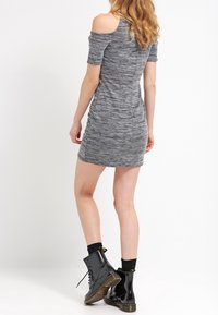 Grå, off-shoulder klänning med kroppsnära passform, texturerad tyg och korta ärmar. Matchad med blanka svarta ankelboots och svarta strumpor.