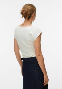 Haut blanc à manches courtes avec un col large, associé à une jupe en denim foncé avec des coutures visibles et un détail de ceinture.