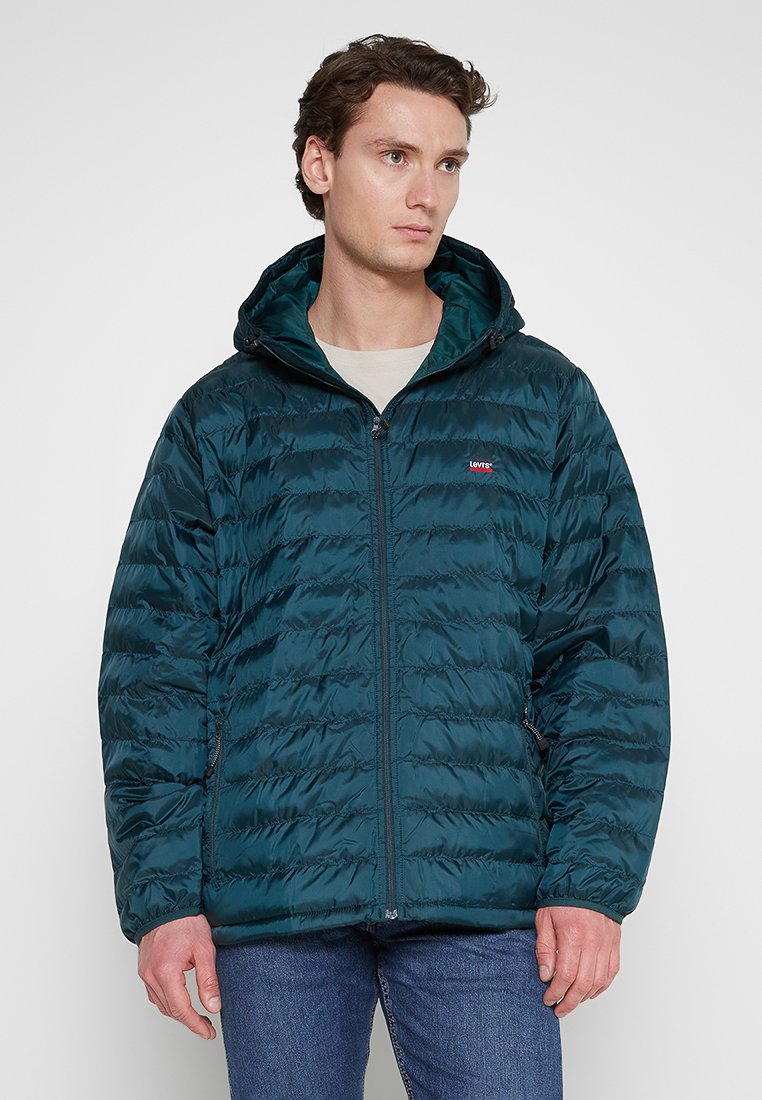 Teal warme luchtige jas met een ritssluiting aan de voorkant, capuchon en horizontaal gestikt patroon. Voorzien van zijzakken en een klein logo op de borst.