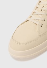 Baskets en cuir crème avec des coutures ton sur ton, un bout arrondi, des lacets plats et une semelle en caoutchouc lisse. Surface texturée avec des accents subtils.