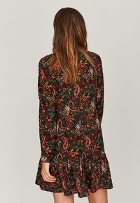 Blumenkleid in Dunkelgrün mit roten, orangefarbenen und weißen Akzenten. Hat lange Ärmel und einen Rüschensaum.