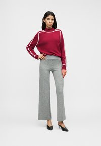 Pull en maille bordeaux avec bordure blanche, associé à un pantalon gris à jambes larges. Chaussures noires à talons. Texture lisse, coupe décontractée, design moderne.