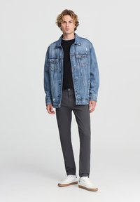 Jasnoniebieska kurtka dżinsowa z dwoma przednimi kieszeniami, noszona na czarnym swetrze. W zestawie z ciemnoszarymi spodniami i białymi trampkami.