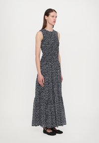 Maxime-kjole med en figursyet overdel, blomsterprint i blått og hvitt på svart bakgrunn, lagvis kant og uten ermer. Svarte flate sko.