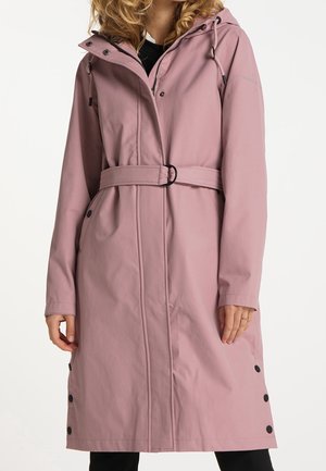 Kobieta w długim, fioletowo-różowym płaszczu z paskiem, kapturem, przednim zamkiem błyskawicznym oraz czarnymi zatrzaskami wzdłuż bocznych szwów.