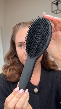 Cepillo de pelo negro con un diseño de paleta ancha, que presenta cerdas cortas y flexibles. Mango suave, acabado mate y texto en relieve en el lateral.