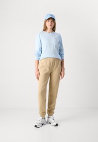 Ljusblå stickad tröja, beige joggingbyxor med elastiskt midjeband, vita träningsskor och en matchande ljusblå keps med logotyp.